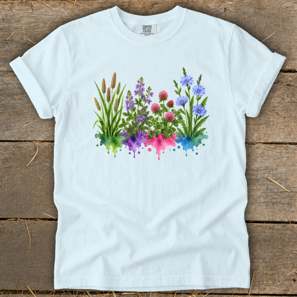 A light blue t-shirt printed with a watercolor illustration of colorful wildflowers over colorful paint splatters.