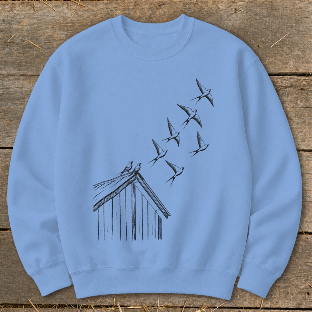 A light blue crewneck sweatshirt featuring a black ink illustration of swallows flying above a rooftop.