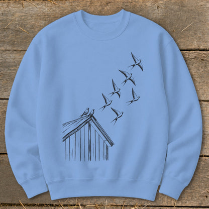 A light blue crewneck sweatshirt featuring a black ink illustration of swallows flying above a rooftop.