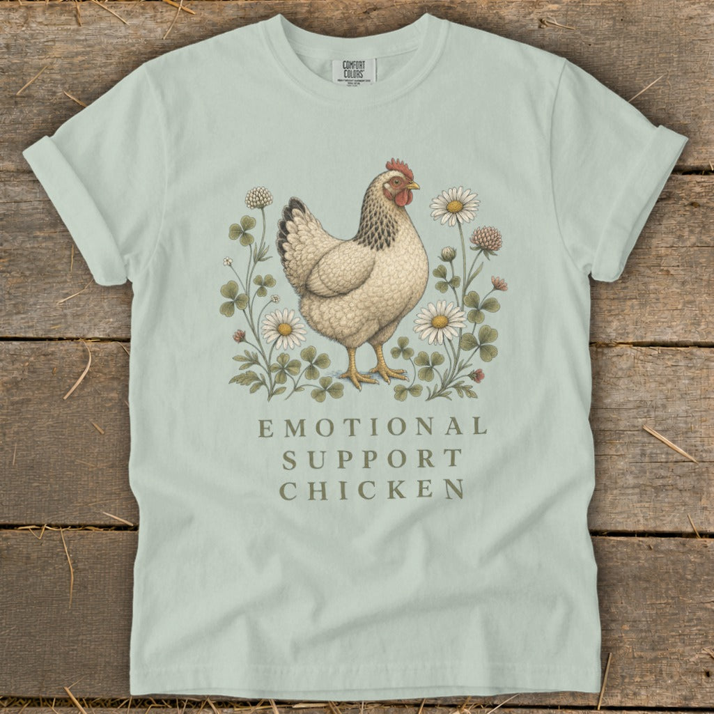 Light blue t-shirt with illustration of a chicken surrounded by clovers and daisies, text reads "Emotional Support Chicken".