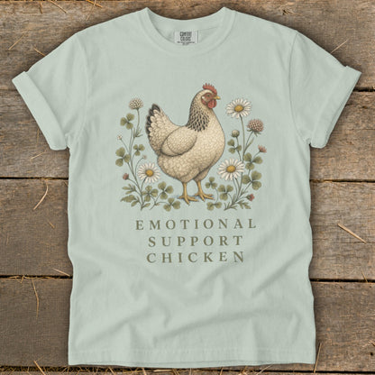 Light blue t-shirt with illustration of a chicken surrounded by clovers and daisies, text reads "Emotional Support Chicken".