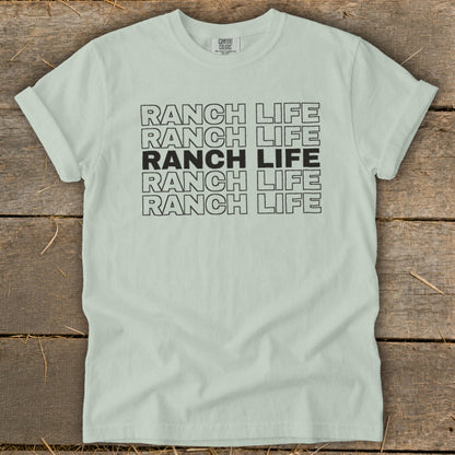Light green t-shirt with repeated outlined text that reads "RANCH LIFE" on a wooden surface.
