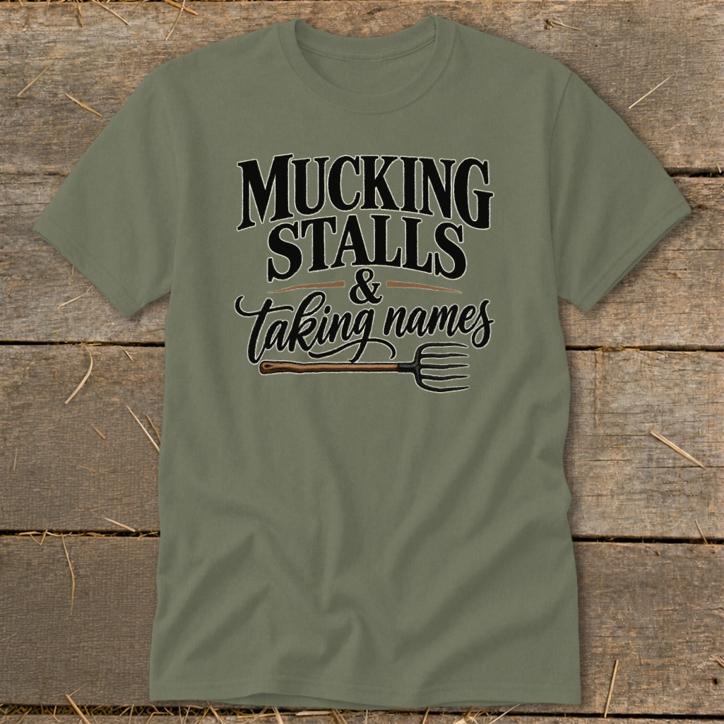 Olive t-shirt with text "MUCKING STALLS & Taking names" and a pitchfork.