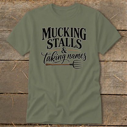 Olive t-shirt with text "MUCKING STALLS & Taking names" and a pitchfork.