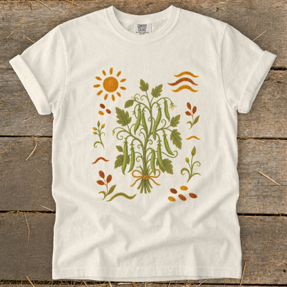 White t-shirt with a central garden illustration of pea pods, sun, and foliage.