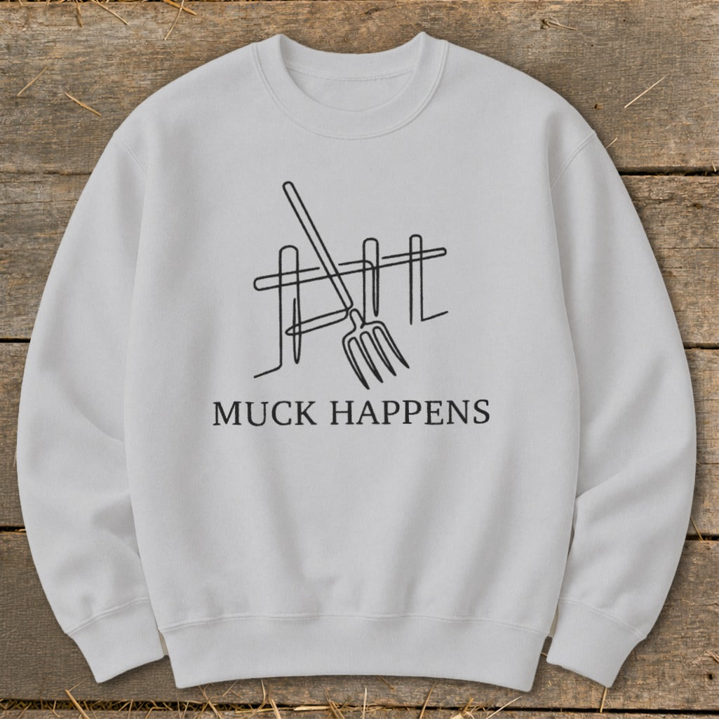 White sweatshirt with "MUCK HAPPENS" text and line art of a pitchfork and fence.