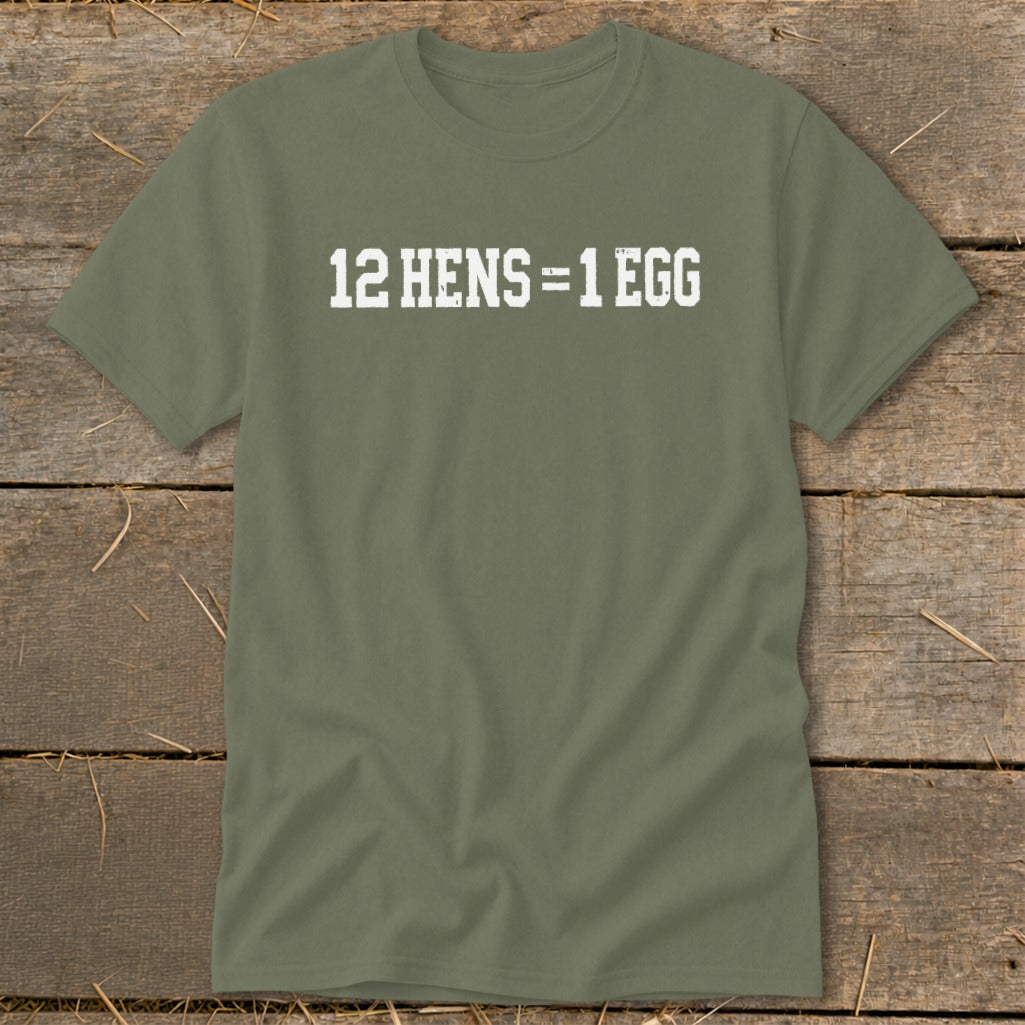An olive green crewneck t-shirt with the white distressed text 12 HENS = 1 EGG printed on the chest, laid flat on a rustic wooden surface.