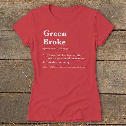 A red women's t-shirt printed with a dictionary definition of Green Broke laid flat on a rustic wooden background.