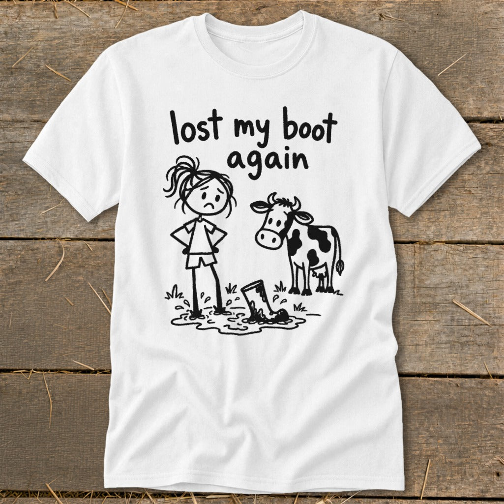 A white short-sleeved t-shirt features a black cartoon graphic of a sad girl, a cow, and text that reads "lost my boot again."