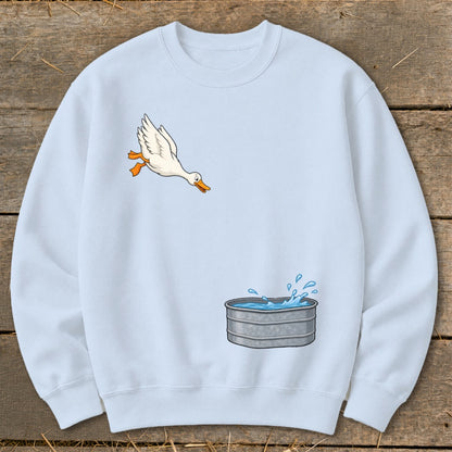 Light blue sweatshirt with a graphic of a duck flying towards a galvanized tub of water.