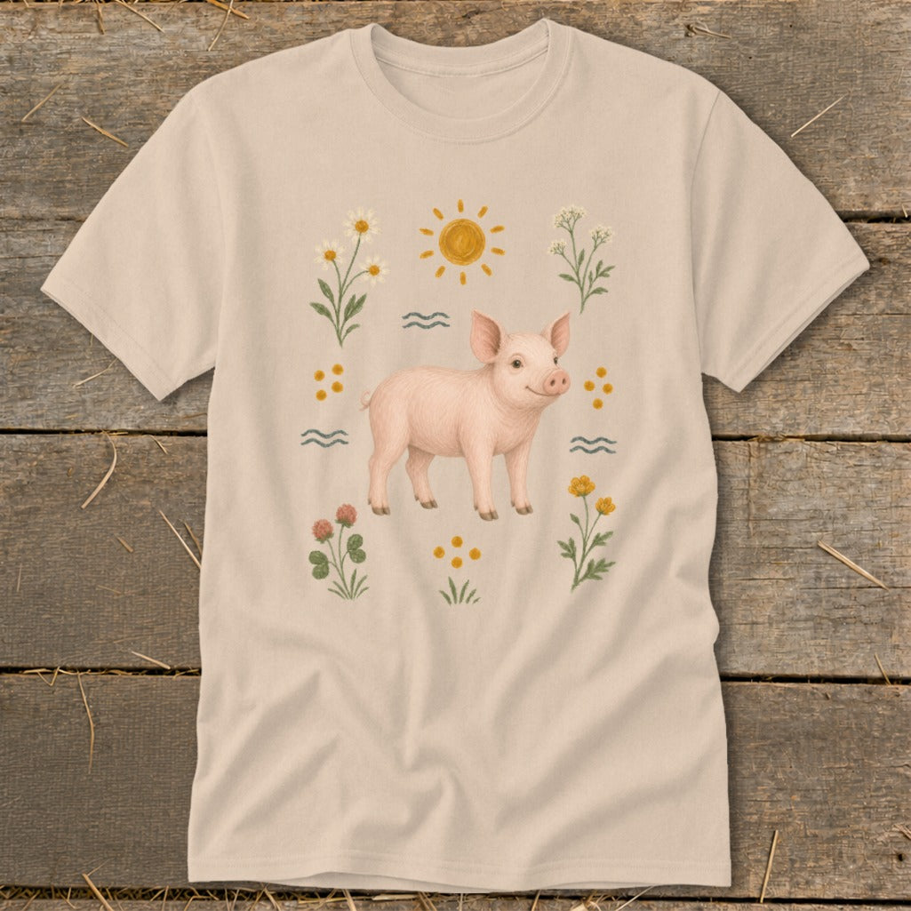 Light tan t-shirt with a watercolor illustration of a piglet surrounded by flowers and a sun.