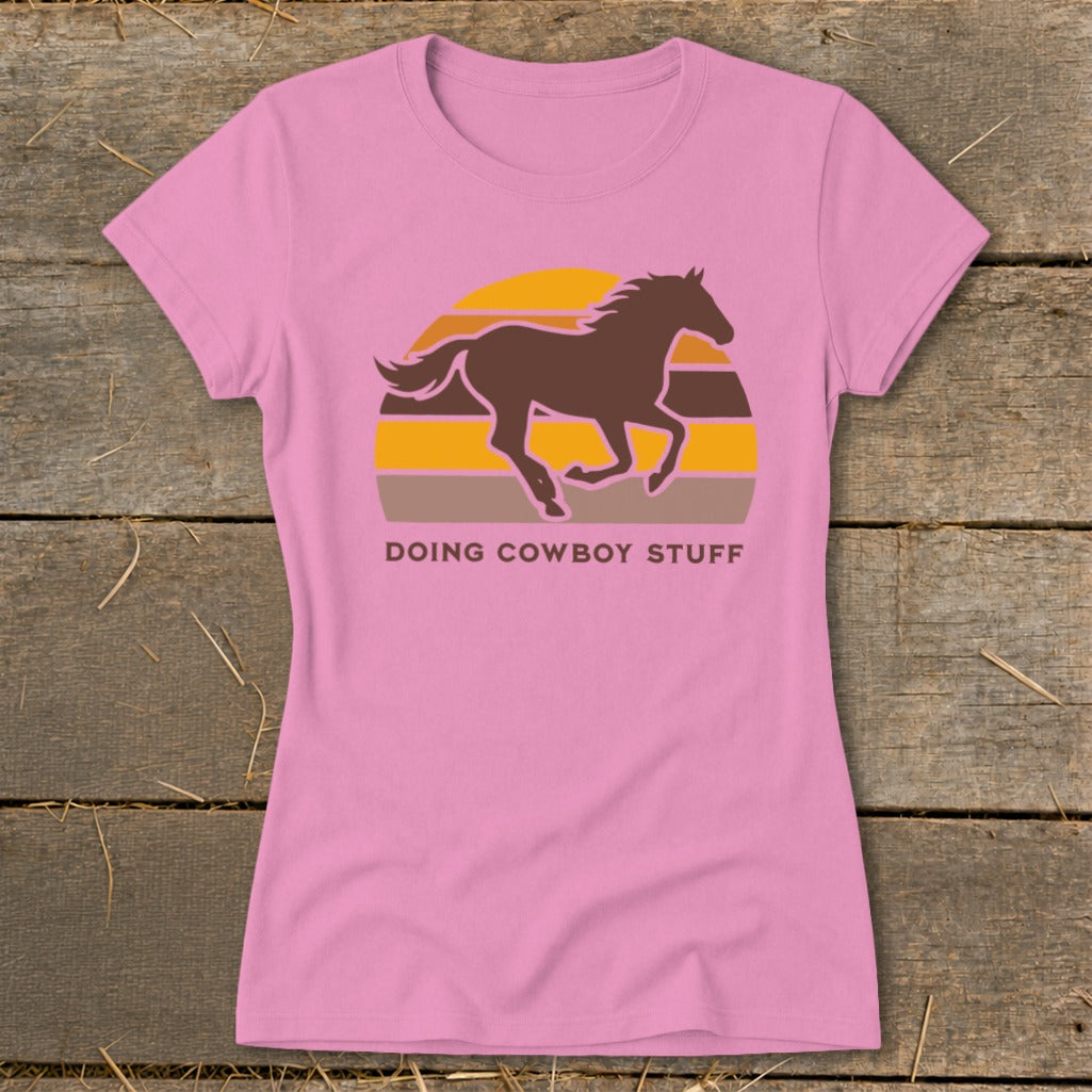 Pink t-shirt with a brown horse silhouette against a sunset graphic and text DOING COWBOY STUFF.