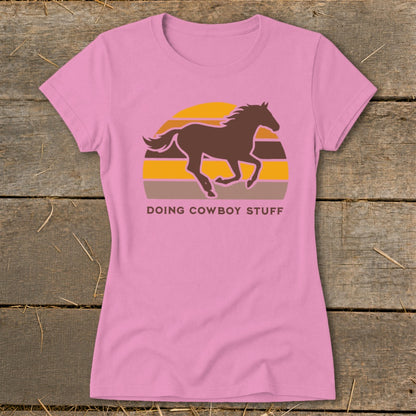 Pink t-shirt with a brown horse silhouette against a sunset graphic and text DOING COWBOY STUFF.