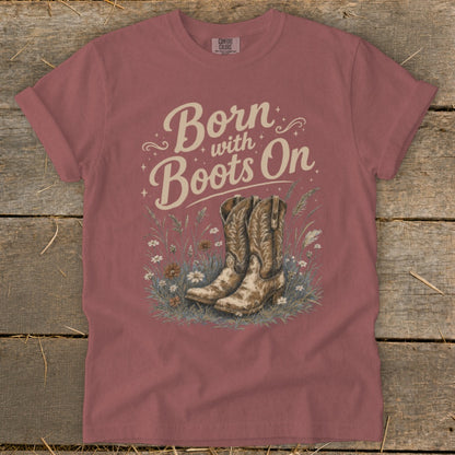 T-shirt graphic with "Born with Boots On" text and cowboy boots in a field.