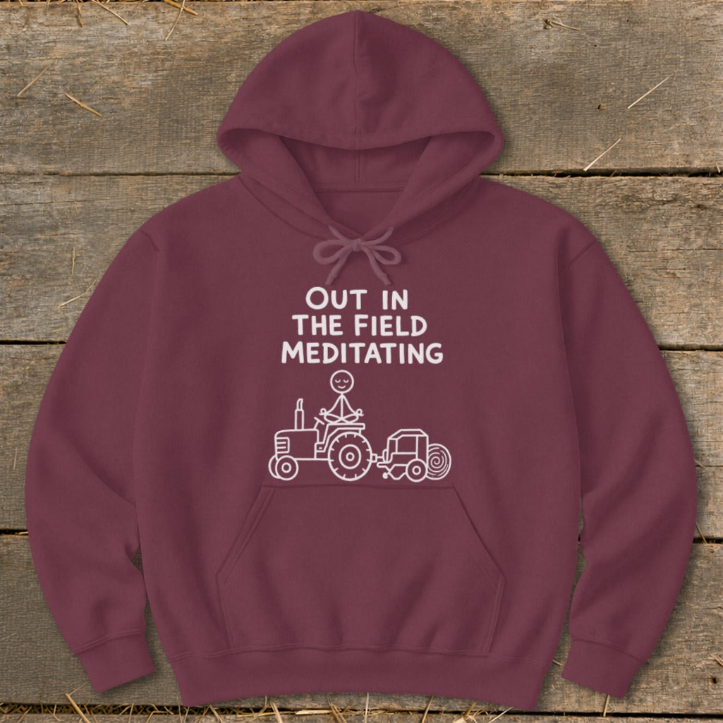Maroon hoodie with text "OUT IN THE FIELD MEDITATING" and a stick figure on a tractor.