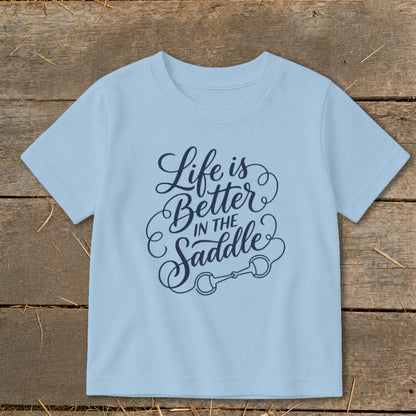 Light blue t-shirt with "Life is Better IN THE Saddle" text and horse bit graphic.