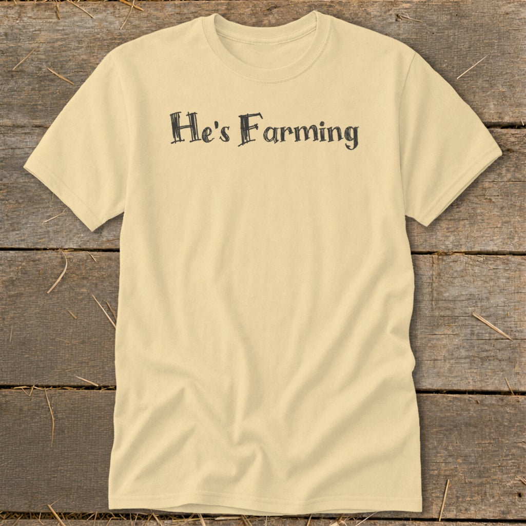 Pale yellow t-shirt with black text reading "He's Farming" centered on chest.