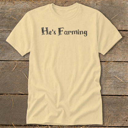 Pale yellow t-shirt with black text reading "He's Farming" centered on chest.