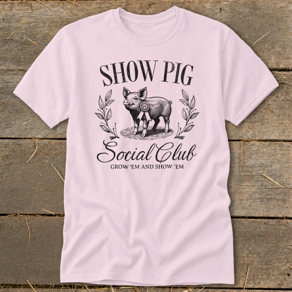 Light pink t-shirt with "SHOW PIG Social Club GROW 'EM AND SHOW 'EM" text and pig graphic.