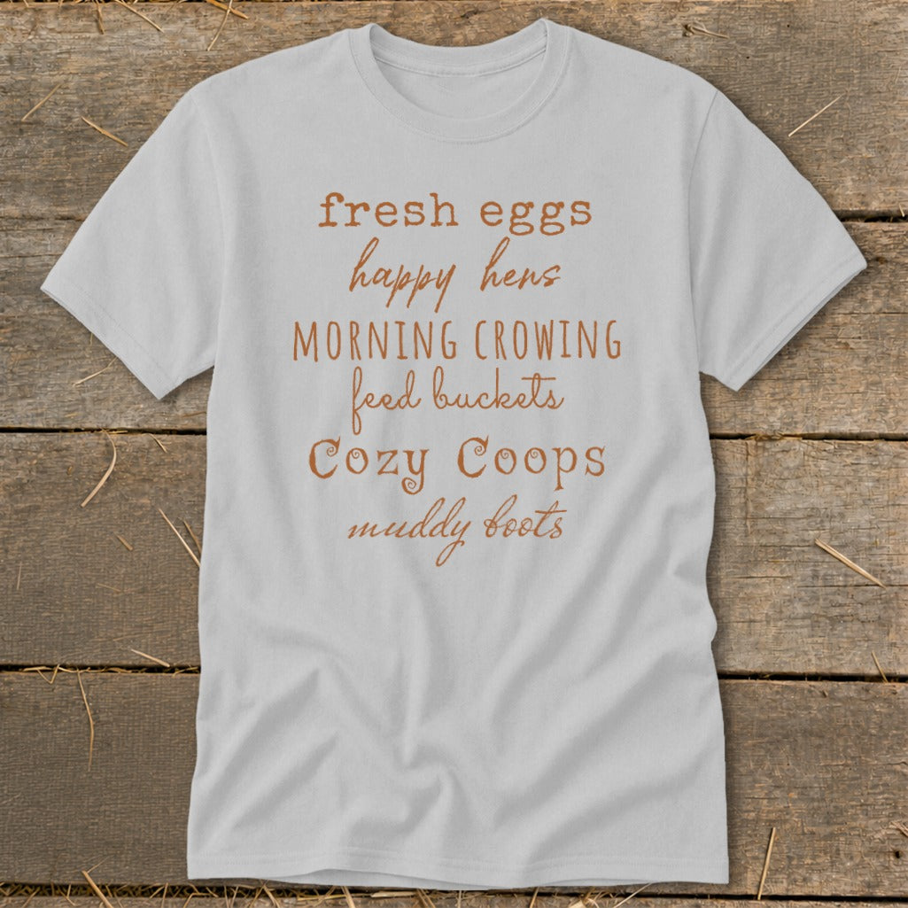 Light gray t-shirt with "fresh eggs happy hens MORNING CROWING feed buckets Cozy Coops muddy boots" text.