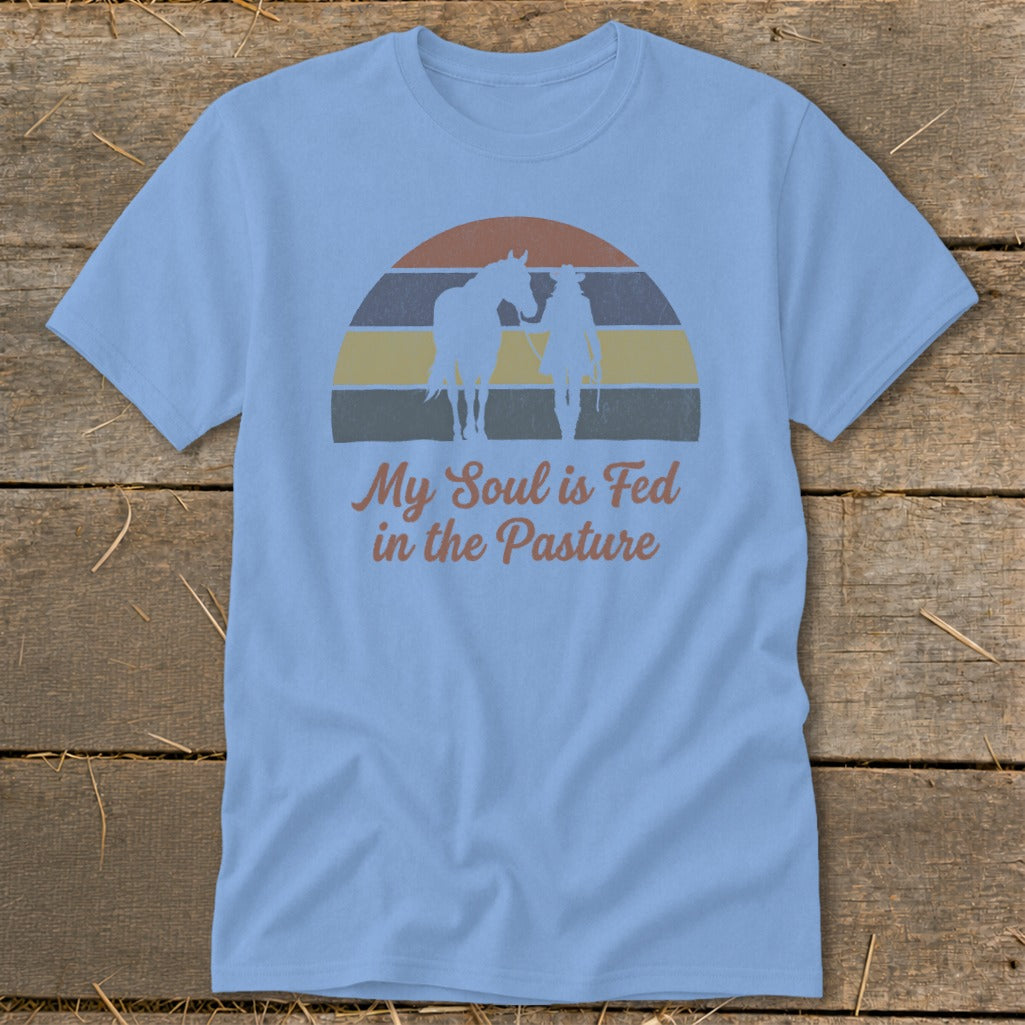 Light blue t-shirt with horse, cowboy, and sunset graphic reading "My Soul is Fed in the Pasture".