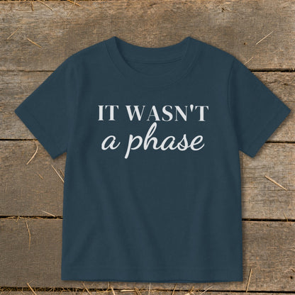 Navy t-shirt with white text "IT WASN'T a phase" on a wooden background.