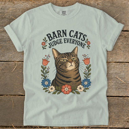 Light blue t-shirt with a tabby cat illustration surrounded by flowers and text "Barn Cats Judge Everyone."