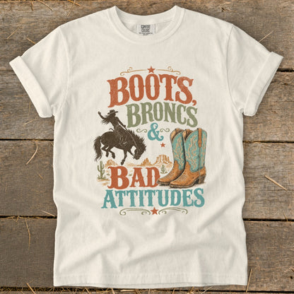 White t-shirt with "Boots, Broncs & Bad Attitudes" graphic featuring cowboy and boots.