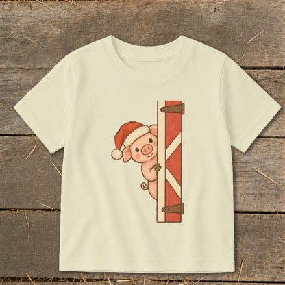 Pig wearing Santa hat peeking from behind a wooden barn door.