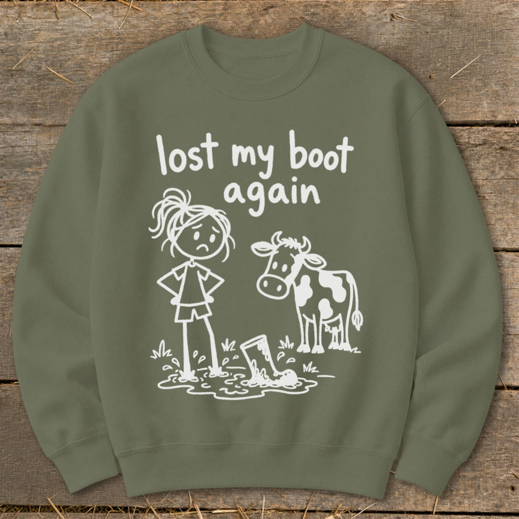 Olive green crewneck sweatshirt featuring a white graphic of a sad stick figure, a cow, and a lost boot in mud with the text lost my boot again.