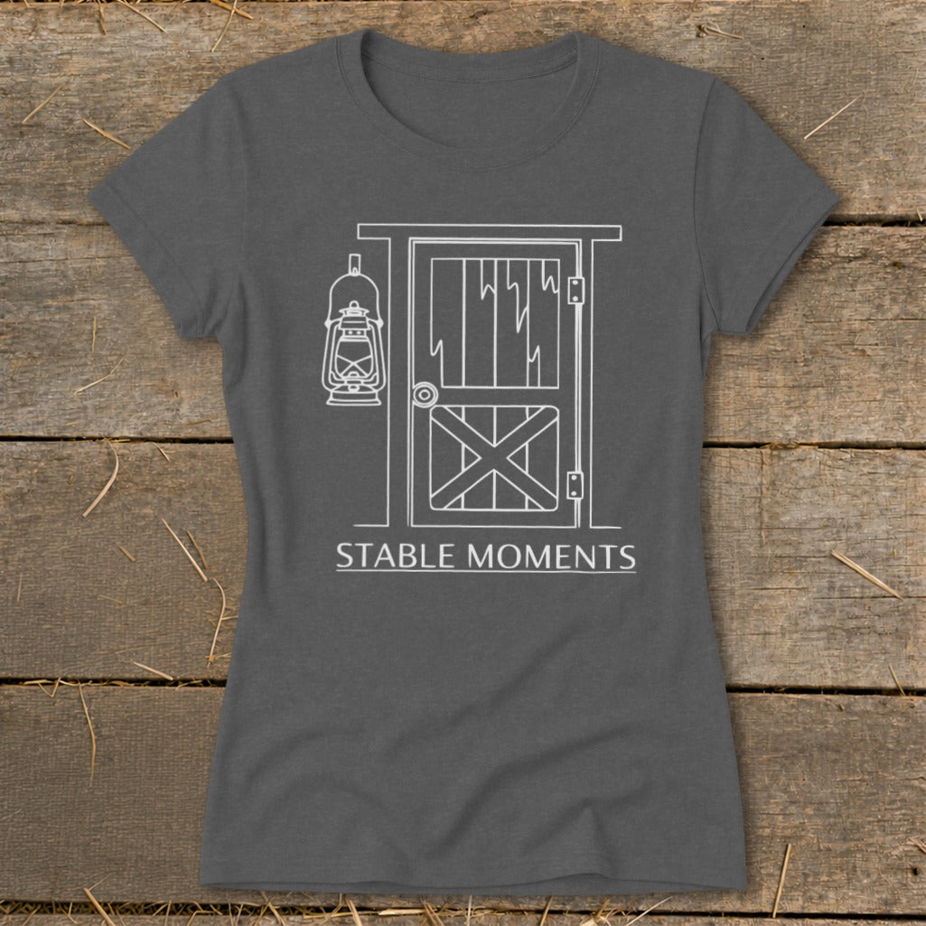 Dark grey t-shirt with white line art of a barn door, hanging lantern, and text "STABLE MOMENTS".