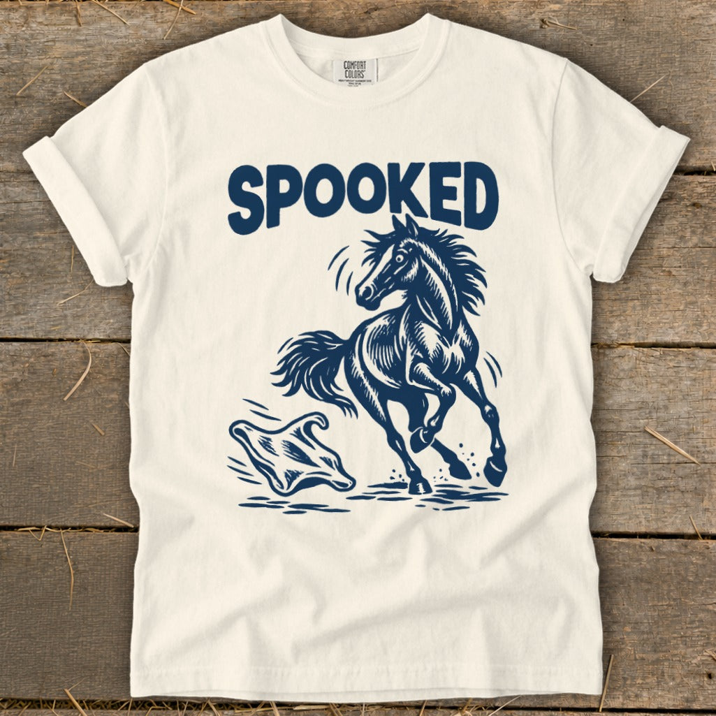 White t-shirt with navy graphic of a startled horse running from a ghost, text reads "SPOOKED".