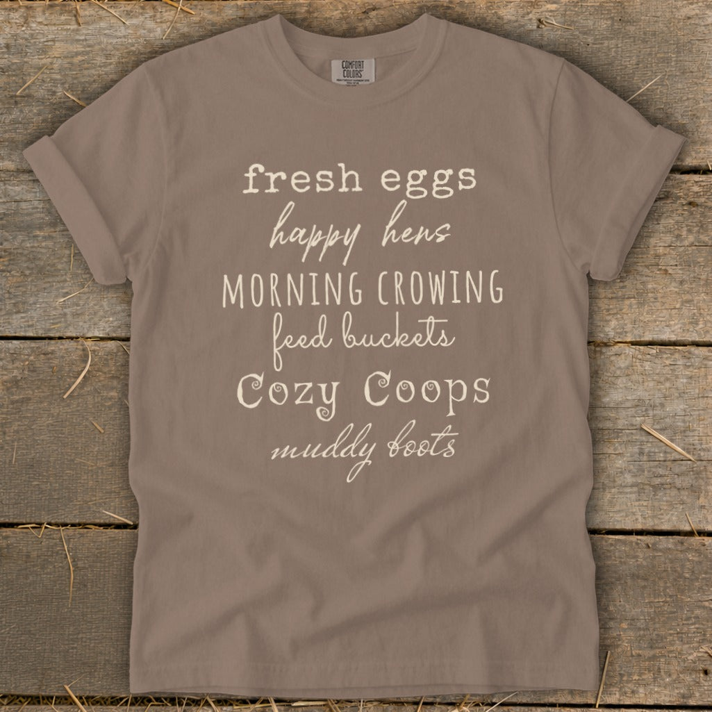 Brown t-shirt with white text: "fresh eggs happy hens MORNING CROWING feed buckets Cozy Coops muddy boots".
