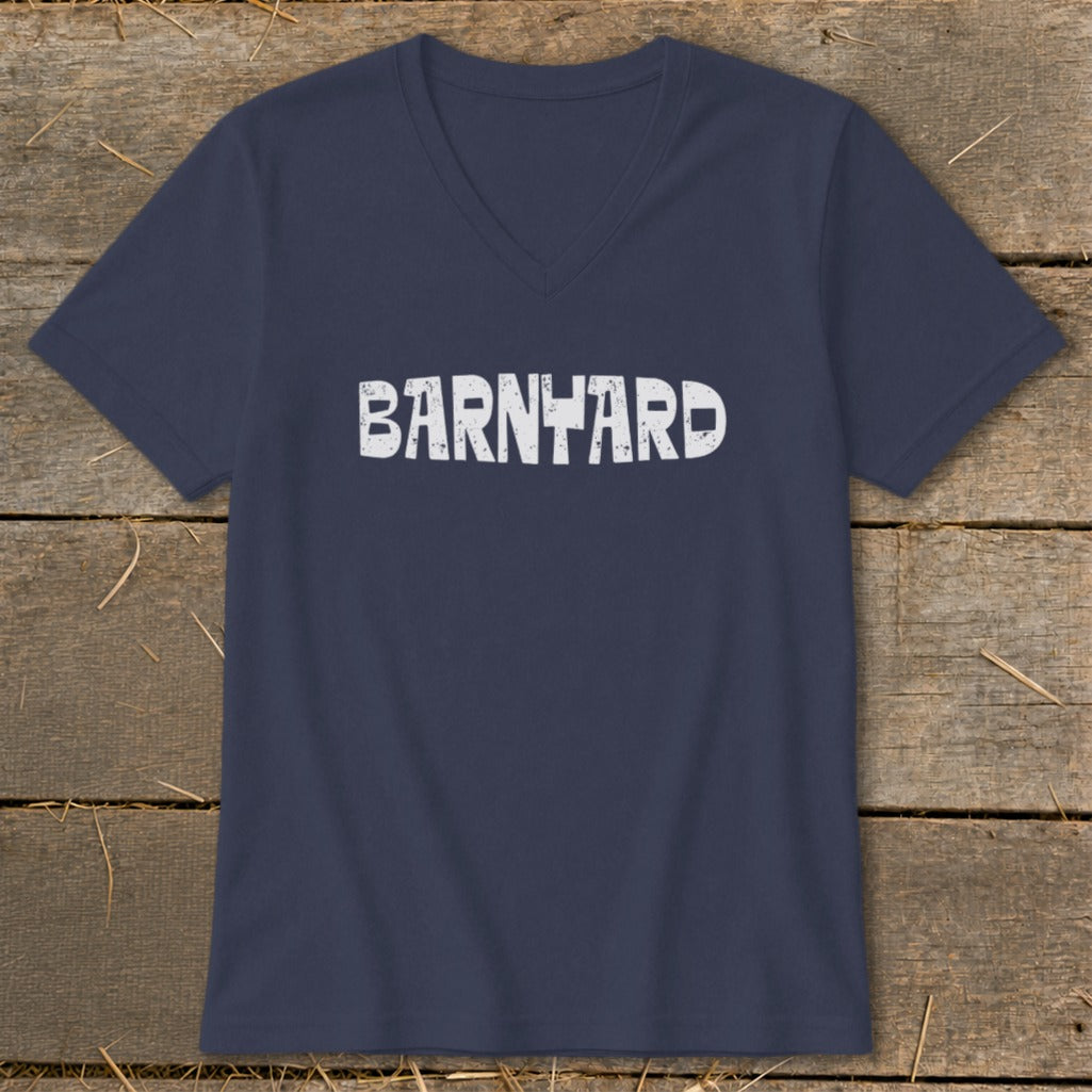 A dark navy blue V-neck t-shirt rests on a rustic wooden background, featuring the distressed white text "BARNYARD" centered on the chest.