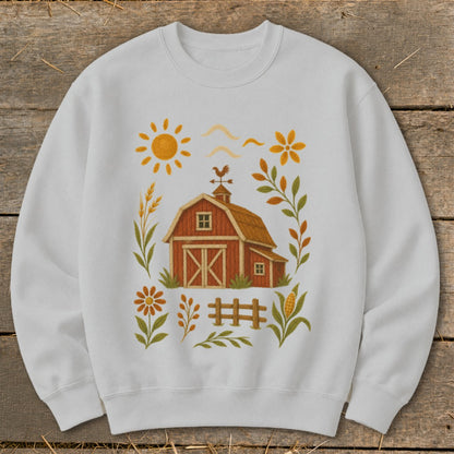 White sweatshirt with a whimsical farm scene featuring a red barn, sun, and autumnal foliage.