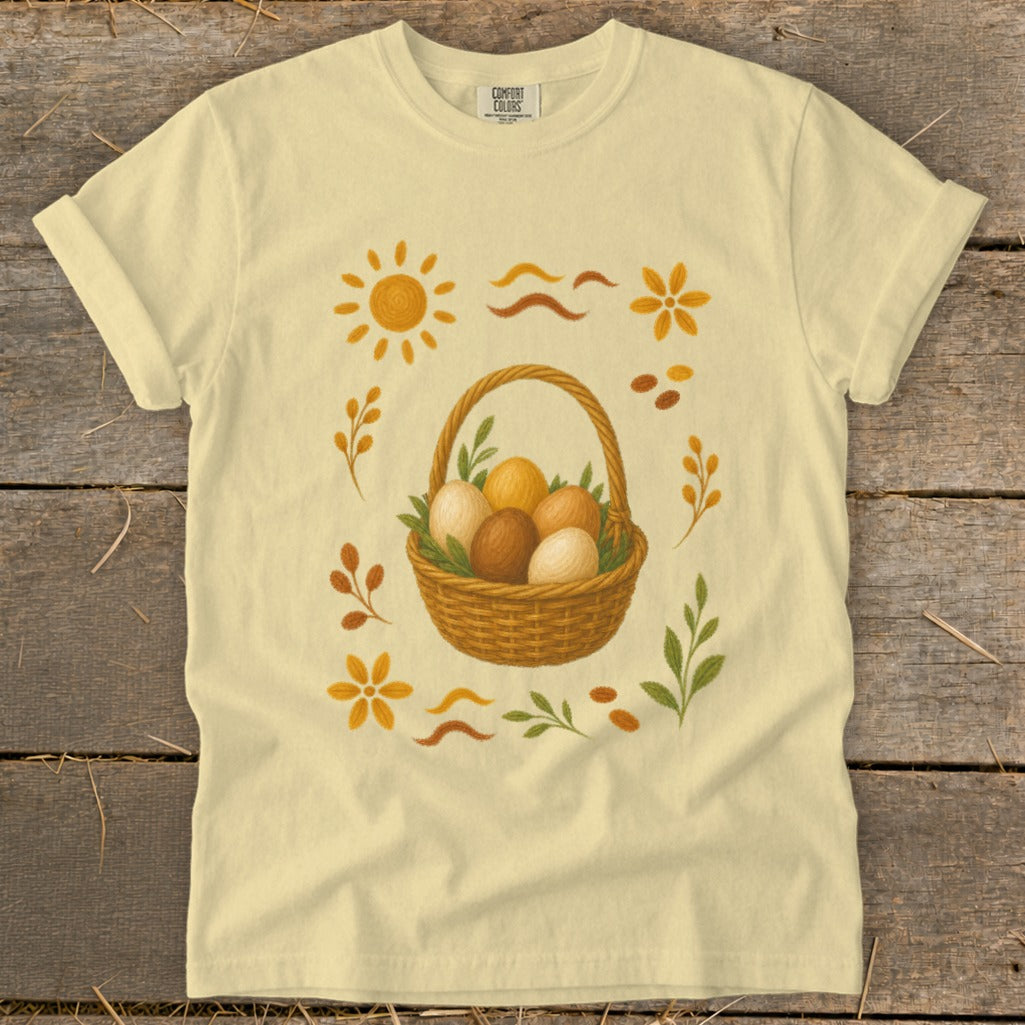 Yellow t-shirt with a wicker basket of eggs and Easter-themed illustrations.