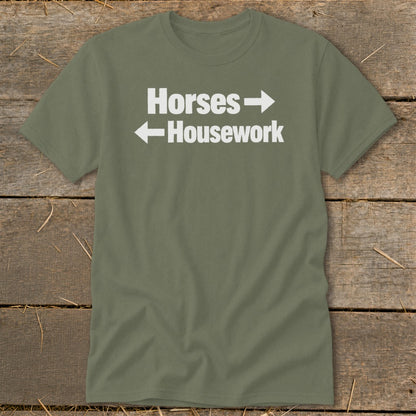 An olive green t-shirt with white text that reads "Horses" with a right-pointing arrow and "Housework" with a left-pointing arrow.