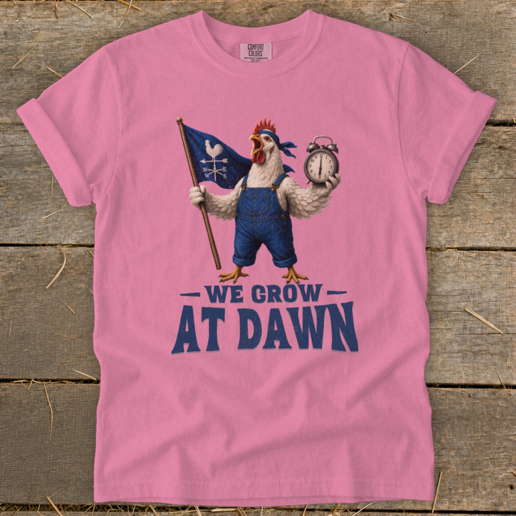 Pink t-shirt with rooster in overalls holding flag and alarm clock, text says "WE GROW AT DAWN".
