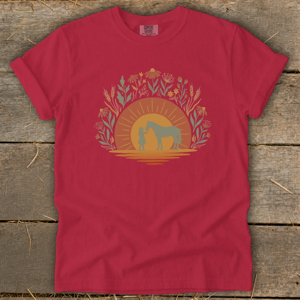 Red t-shirt with a graphic of a person and horse at sunset surrounded by flowers.