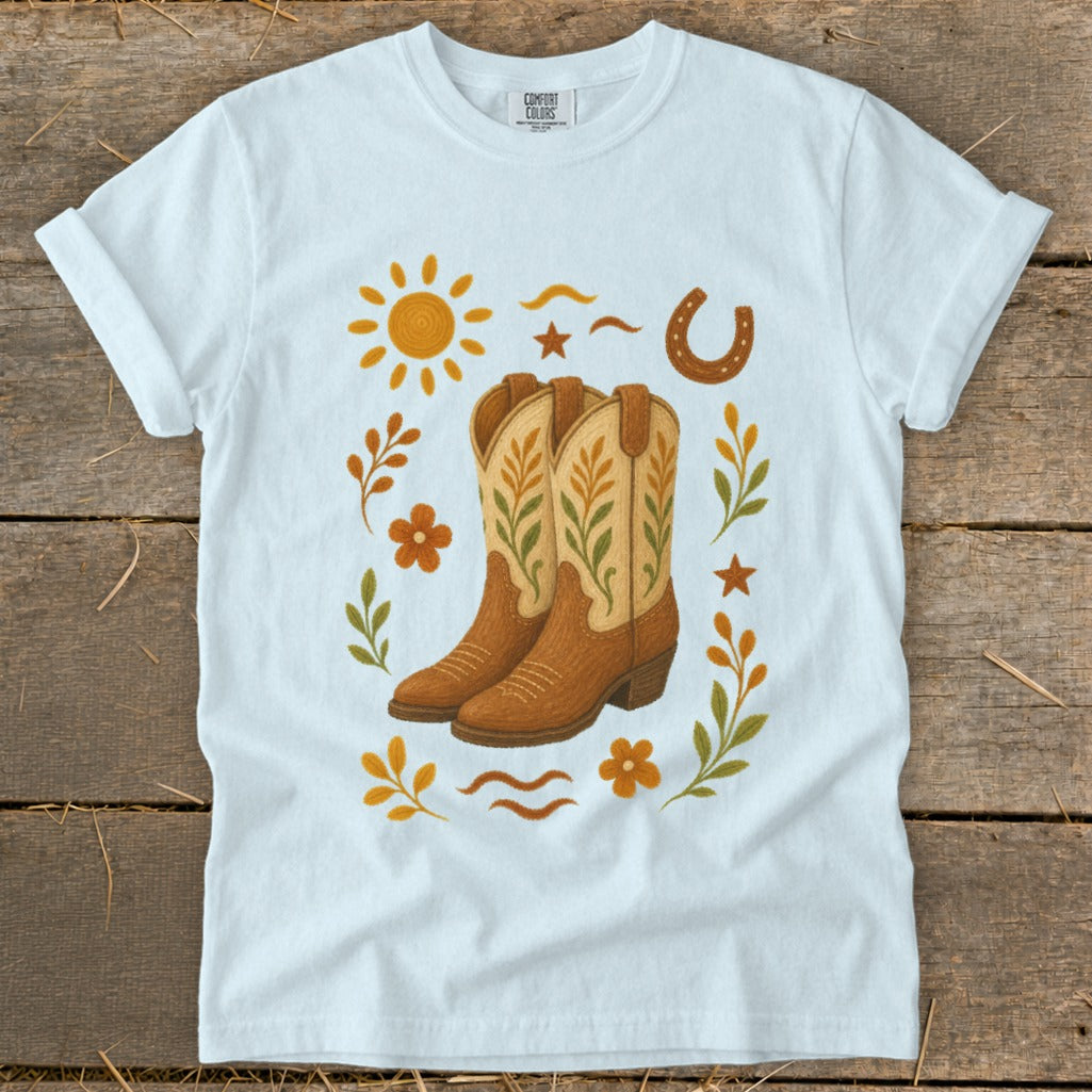 White t-shirt with cowboy boots, sun, horseshoe, flowers, and stars graphic.