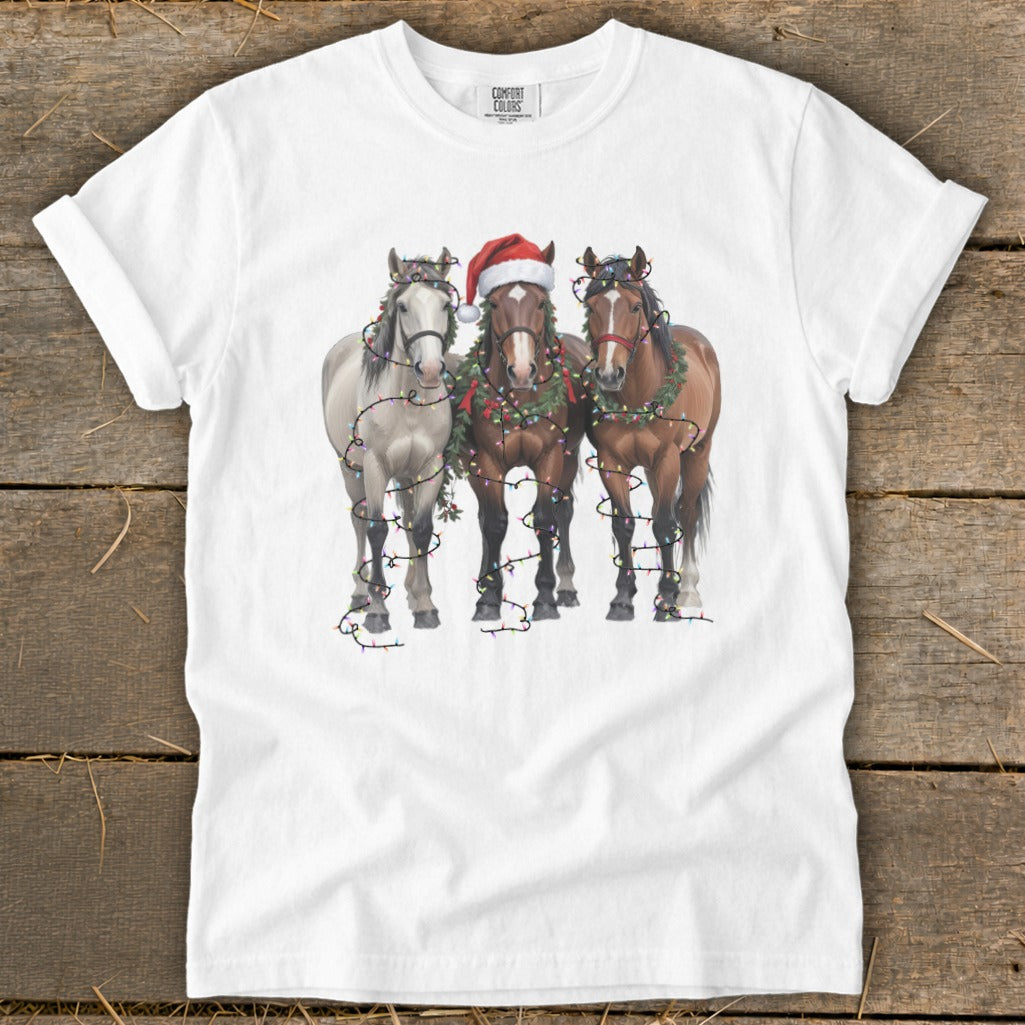 Three horses wearing Christmas lights and garlands, one with a Santa hat.