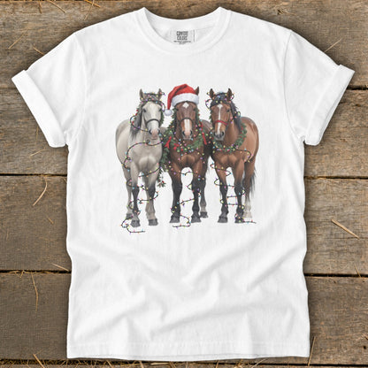 Three horses wearing Christmas lights and garlands, one with a Santa hat.