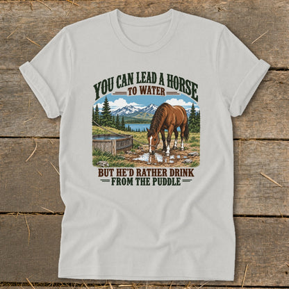 A light gray t-shirt featuring a graphic of a horse drinking from a puddle with humorous text.