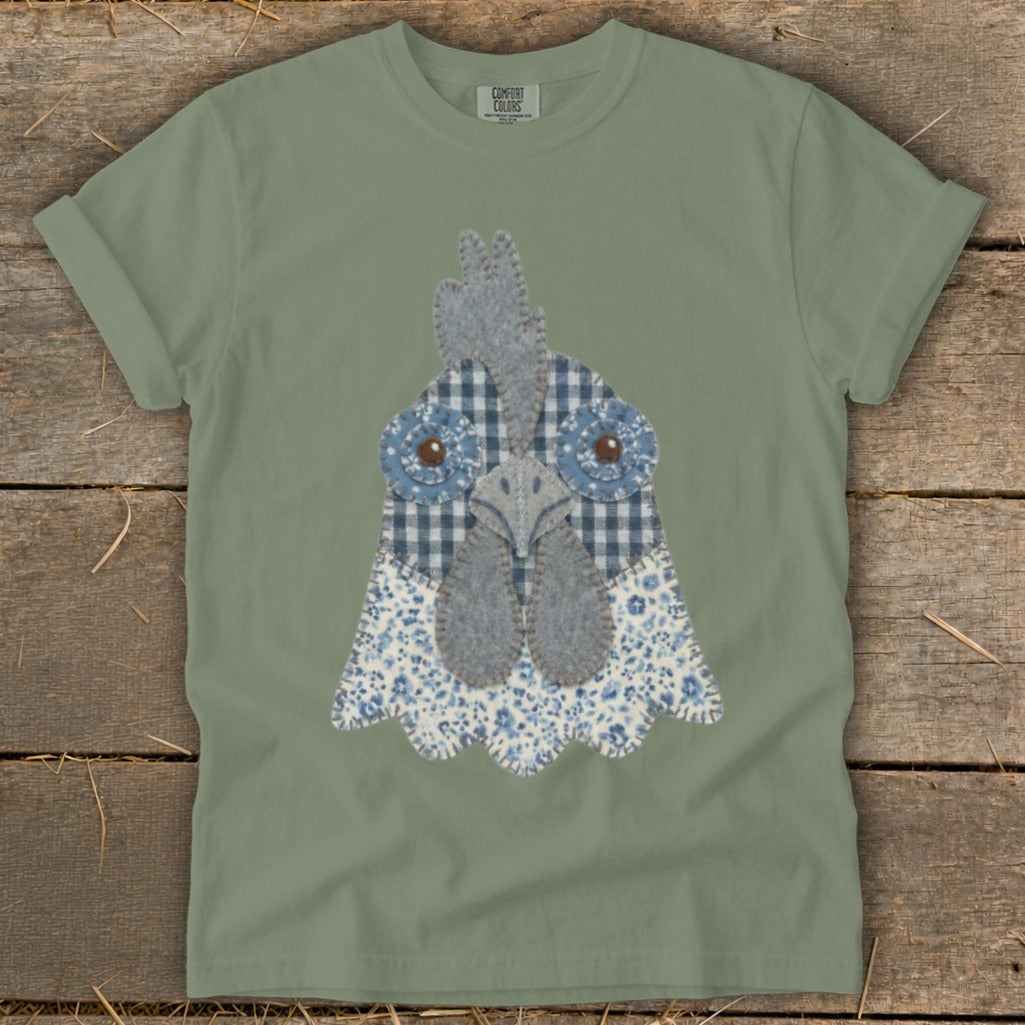Sage green t-shirt with a blue and white fabric chicken head applique.