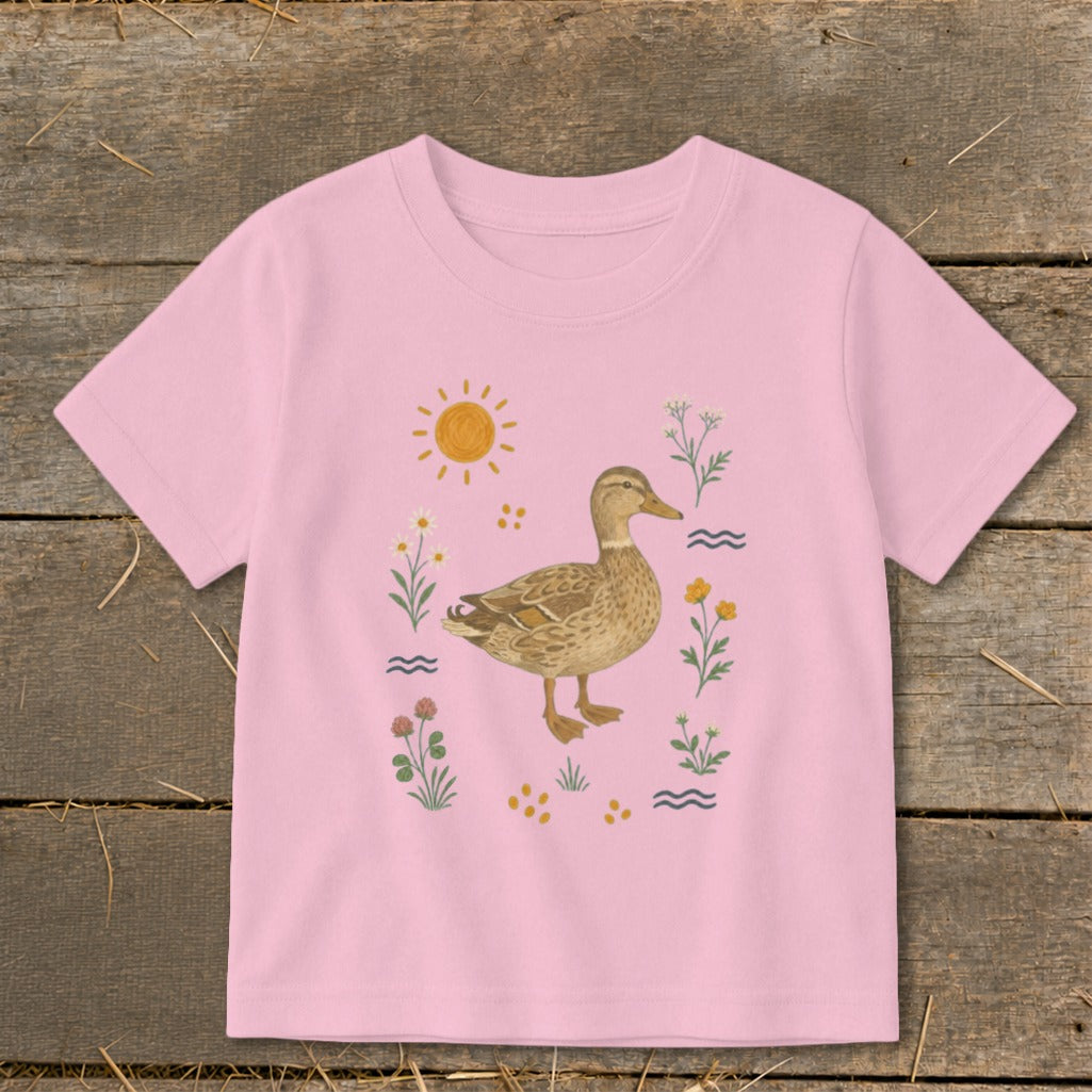 Pink t-shirt with a watercolor illustration of a mallard duck surrounded by flowers and sun.