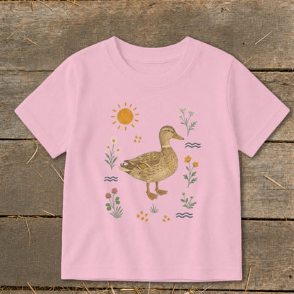 Pink t-shirt with a watercolor illustration of a mallard duck surrounded by flowers and sun.