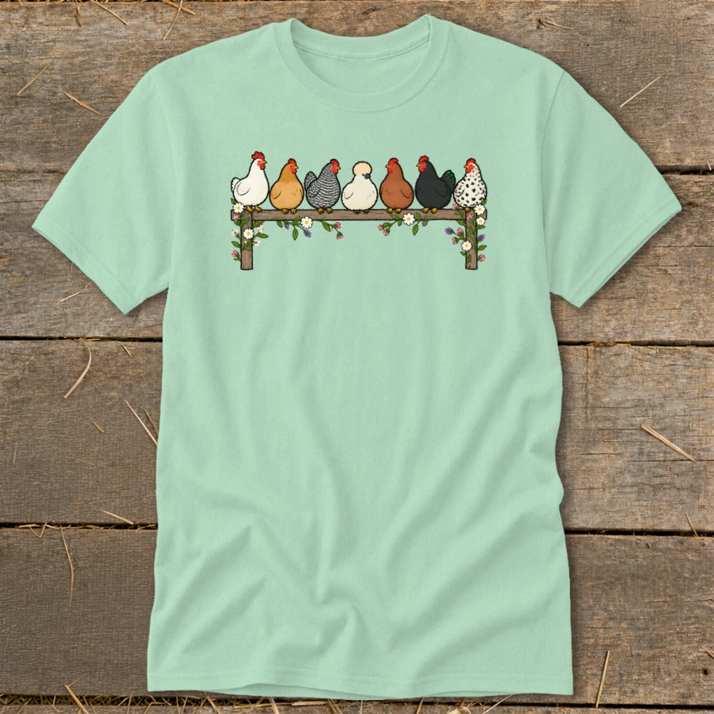 Mint green t-shirt featuring an illustration of seven colorful chickens sitting on a flower-decorated fence.