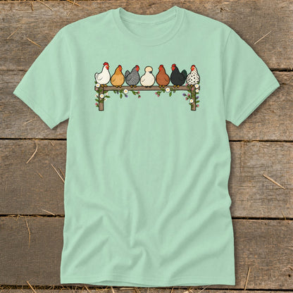 Mint green t-shirt featuring an illustration of seven colorful chickens sitting on a flower-decorated fence.