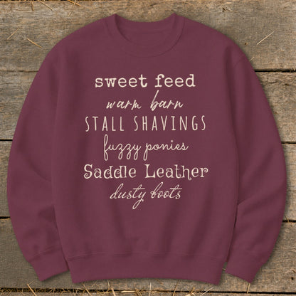 Maroon sweatshirt with text "sweet feed warm barn STALL SHAVINGS fuzzy ponies Saddle Leather dusty boots".