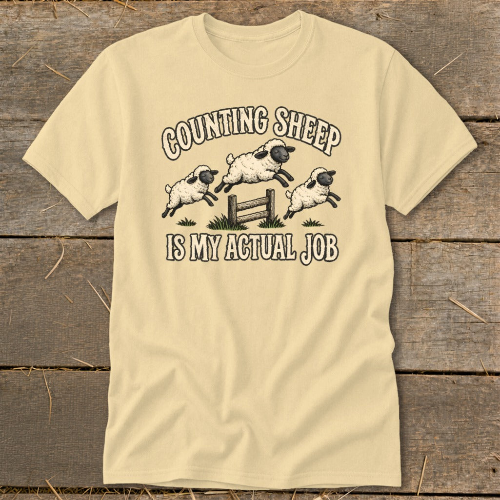 Cream t-shirt with cartoon sheep jumping over a fence, text reads "Counting Sheep Is My Actual Job".